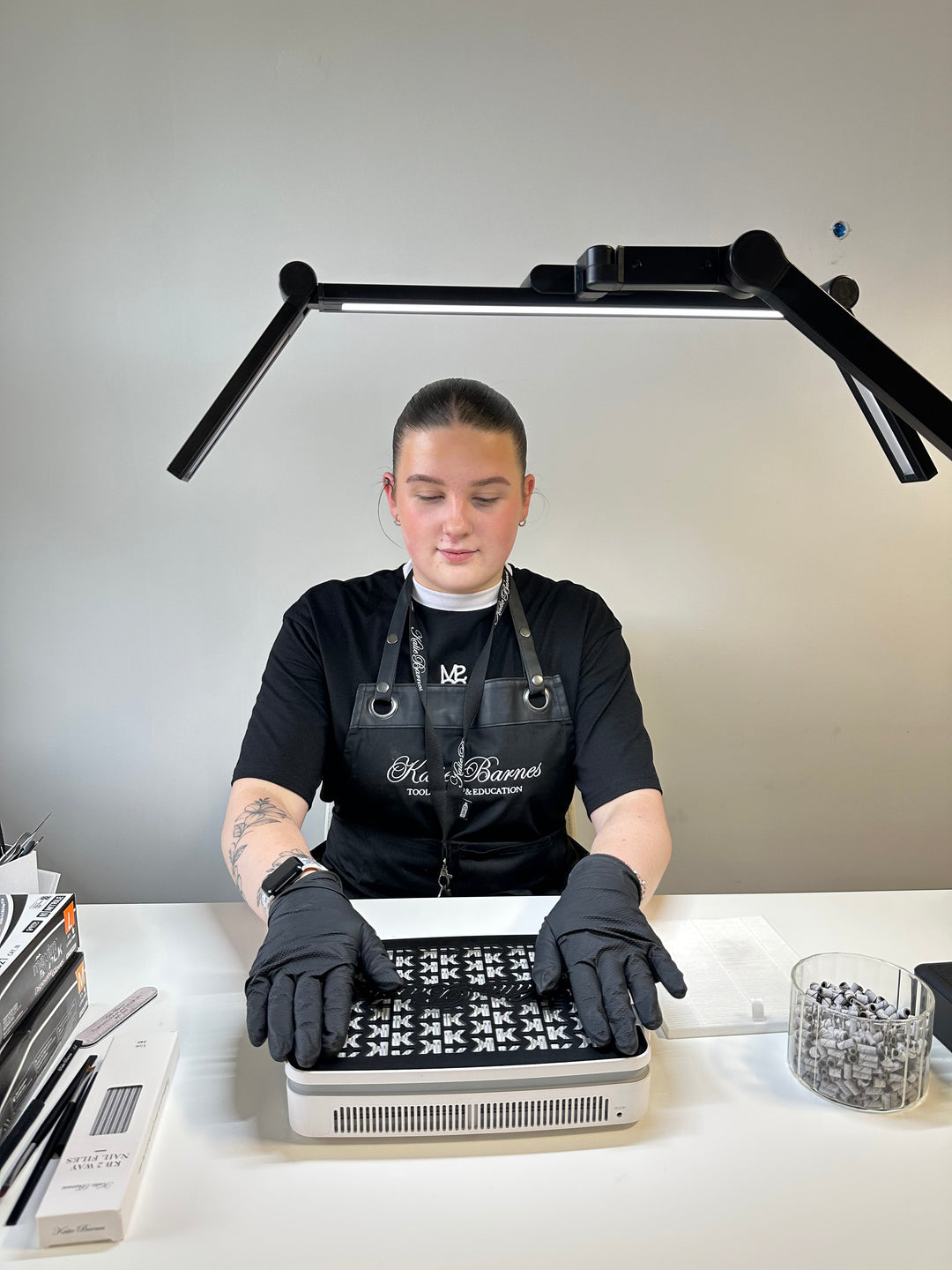 Nail technician wearing Katie Barnes Black Apron with hands on Katie Barnes Dust Collector
